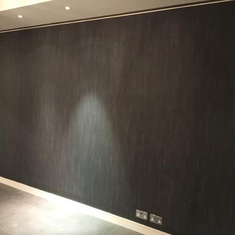 A large, dark charcoal textured accent wall professionally finished by a painter and decorator. The image shows clean edges against a white ceiling and skirting boards in a modern London interior, demonstrating high-end workmanship available across Canary Wharf, Islington, and Covent Garden.