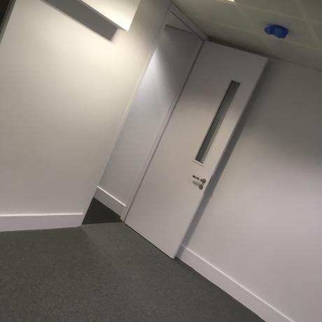A professionally painted modern office interior featuring clean white walls, a satin-finish door with a glass panel, and white skirting boards. High-quality commercial decorating work for businesses in Canary Wharf, Islington, and Covent Garden.