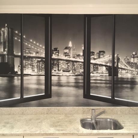 A large black and white cityscape mural featuring a bridge and city skyline at night, professionally installed behind a kitchen countertop. Expert wallpaper and mural hanging services provided across Canary Wharf, Islington, and Covent Garden.
