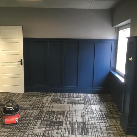A professional interior finish featuring deep navy blue wall panelling against a light grey upper wall in a modern office. The image highlights precise wood panelling work and clean paint lines, showcasing specialist decorating services in Canary Wharf, Islington, and Covent Garden.