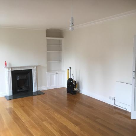A spacious living room featuring professionally painted off-white walls, a classic marble fireplace with a black insert, and built-in alcove shelving. The high-quality finish on the woodwork and decorative coving highlights specialist decorating services available in Islington, Covent Garden, and Canary Wharf.