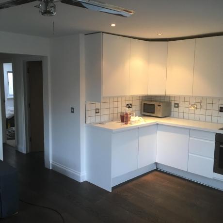 A contemporary kitchen area featuring professionally painted white walls and matching white cabinetry. The image showcases high-quality finishes on the skirting boards and around tiled splashbacks, reflecting expert decorating services in Islington, Covent Garden, and Canary Wharf.