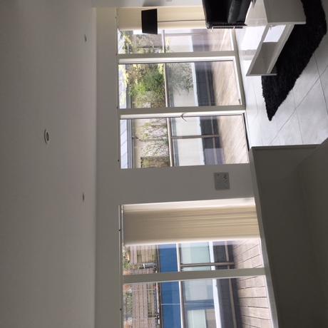 bright, contemporary living space featuring professionally painted white walls and ceiling. The image showcases clean finishes around large floor-to-ceiling windows and doors leading to a private terrace, reflecting high-end decorating services in Canary Wharf, Islington, and Covent Garden.