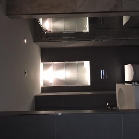 A sleek, modern bathroom featuring dark grey tiled walls and integrated glass shelving with soft recessed lighting. The space includes a contemporary white wall-hung toilet and vanity unit, showcasing high-end interior finishing services in Canary Wharf, Islington, and Covent Garden.