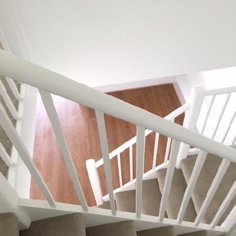 A high-angle view of a professionally painted white staircase and banister with neutral carpeting. The image highlights clean, crisp finishes on internal woodwork, reflecting expert decorating services in Islington, Canary Wharf, and Covent Garden.