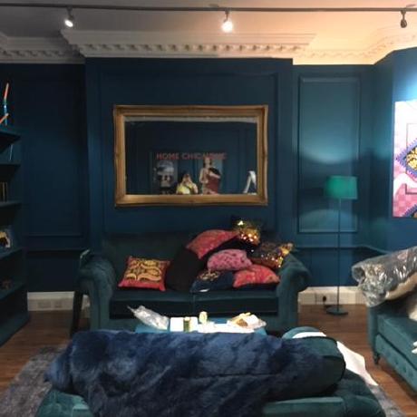 A sophisticated living room featuring deep teal painted walls with decorative wall panelling and ornate white ceiling coving.