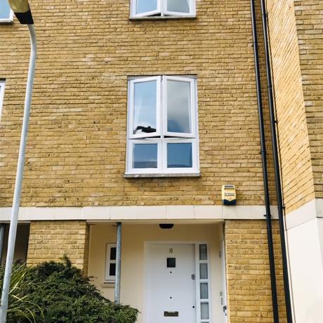 The exterior of a modern yellow-brick townhouse featuring a professionally painted white front door and matching white window frames. The image highlights clean, weather-resistant finishes on exterior woodwork, showcasing expert residential maintenance and decorating services