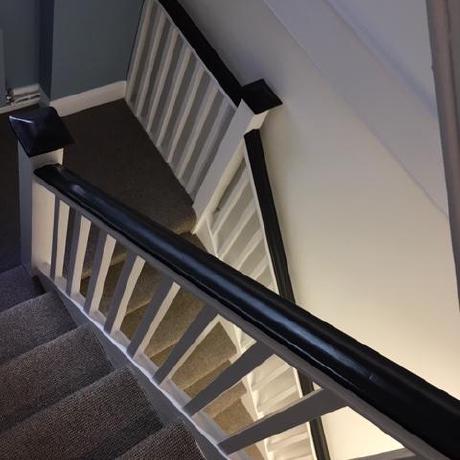 A close-up, high-angle view of a professionally painted period staircase featuring crisp white spindles and a contrasting black satin-finish handrail. The image showcases expert attention to detail on internal woodwork and banister restoration in Islington, Covent Garden, and Canary Wharf.