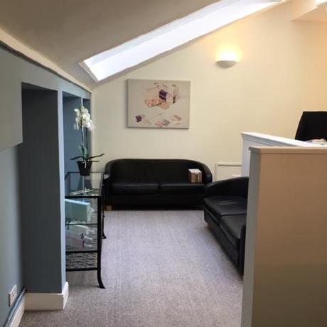 A professionally decorated office waiting area featuring slanted ceilings with integrated skylights and crisp white painted walls. The space includes soft blue accent walls, a neutral grey carpet, and black leather seating, showcasing high-quality commercial interior finishing