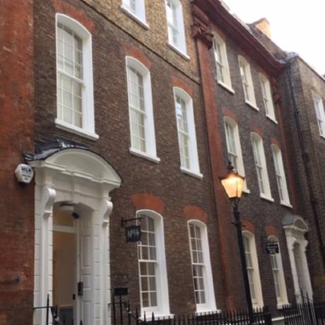 The exterior of a traditional brick period townhouse featuring professionally painted white sash windows and an ornate white front door surround. The image showcases high-quality exterior decorating and maintenance for historic buildings in Covent Garden, Islington, and Canary Wharf.