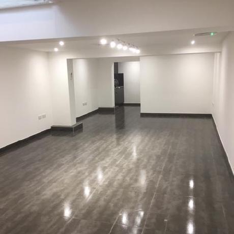 A spacious, open-plan commercial interior featuring professionally painted crisp white walls and ceiling. The space is accented by a high-gloss polished grey floor and modern spotlighting, showcasing premium interior decorating services for businesses in Canary Wharf, Islington, and Covent Garden.