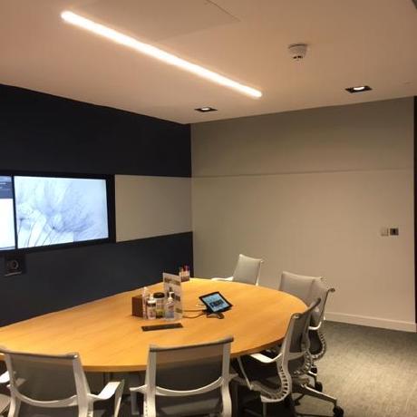 A professional executive boardroom featuring a multi-tone feature wall in navy blue, light grey, and white with an integrated media screen. The space is finished with an oval light wood conference table, modern ergonomic seating, and recessed LED strip lighting, showcasing high-end commercial decorating